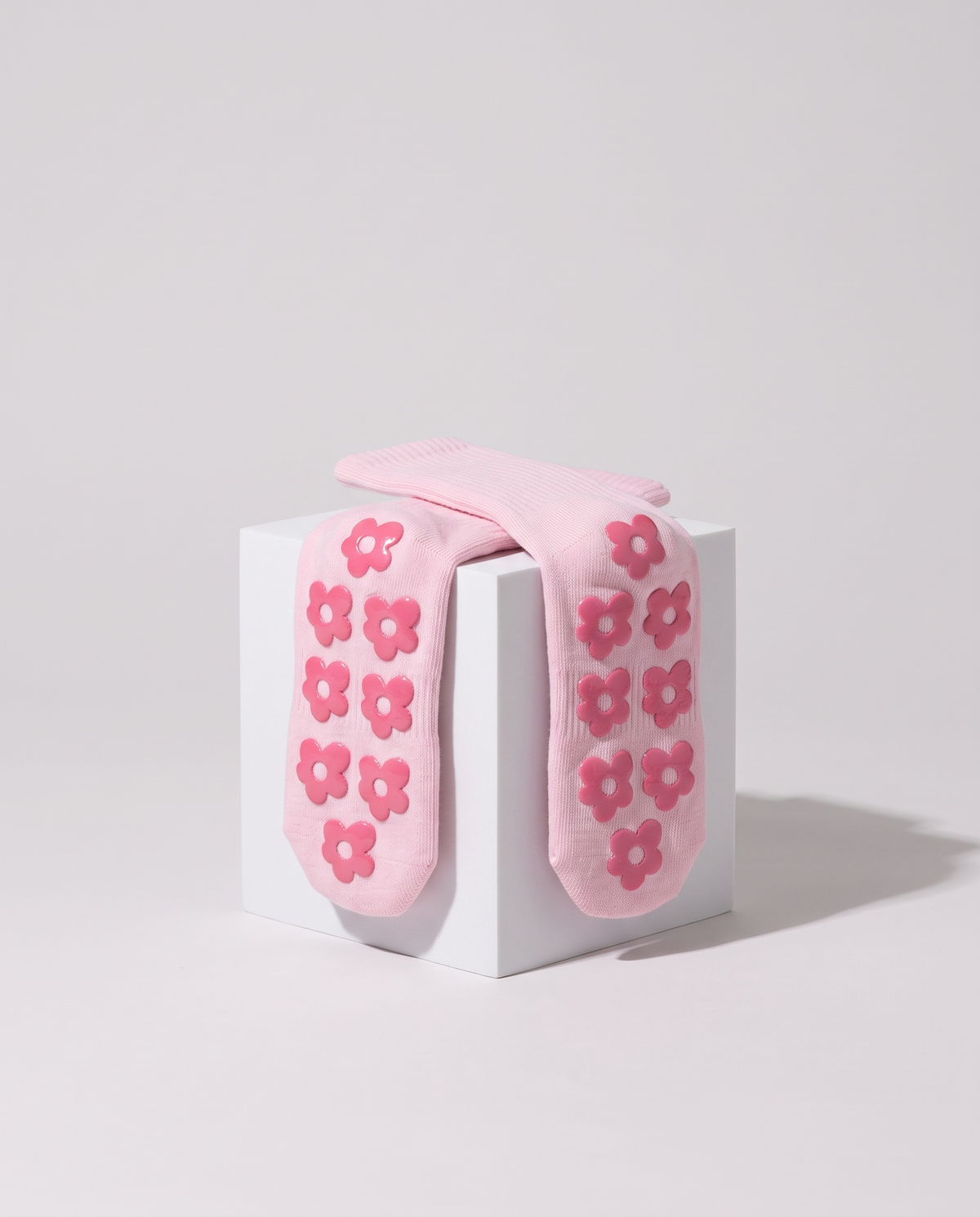 Pink balanced. grip socks draped over a white cube showing the rose flower grips