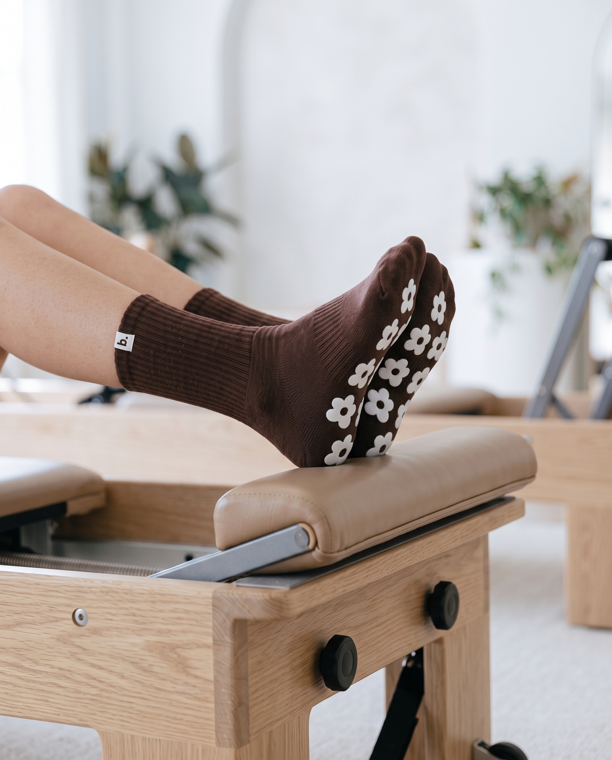 Feet in brown balanced. grip socks resting on a pilates reformer footbar in a bright studio